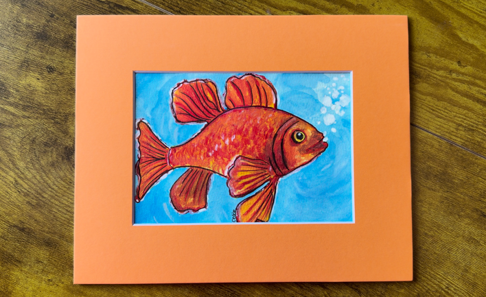 Hand-painted watercolor goldfish painting — a bright orange goldfish in bubbly blue water, matted in orange, by Céline
